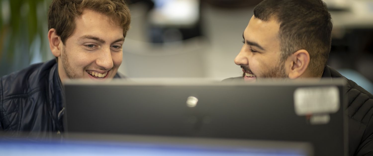 Students in classroom Two male students smile over a computer